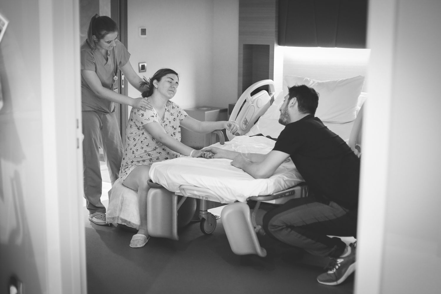 A medical scene in black and white shows a patient in a hospital bed while healthcare staff attend to them. Birth photos