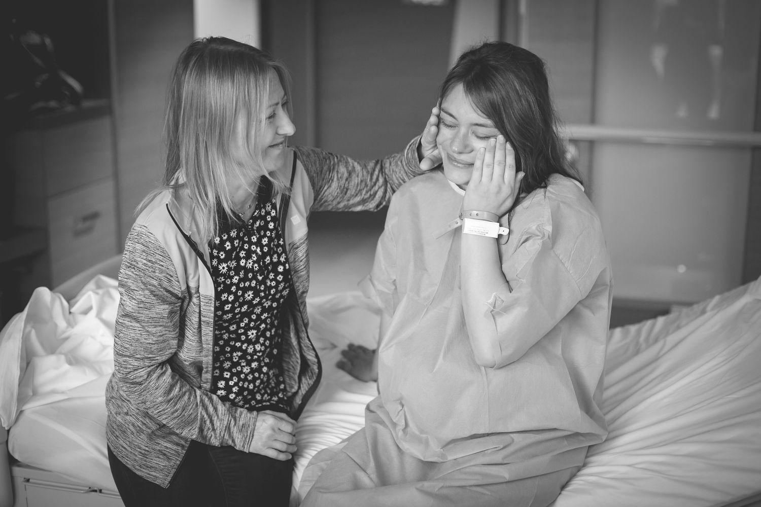 Two friends share a lighthearted moment while sitting together in a black and white photograph.