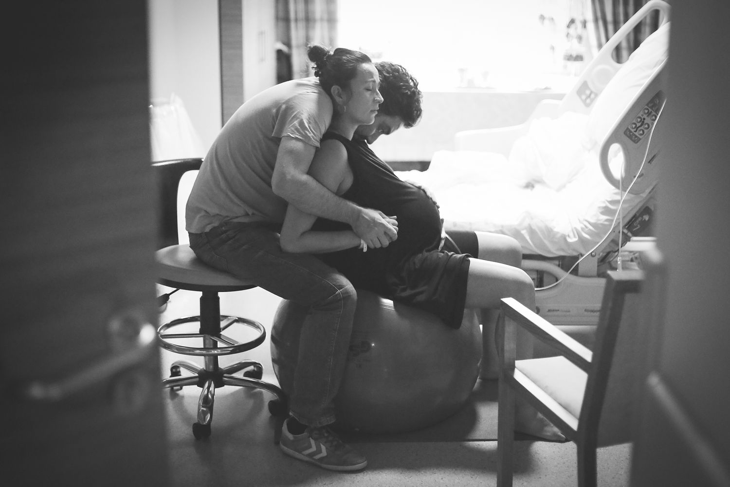 Black and white intimate photograph of a couple sharing a tender moment while seated in a clinical setting.
