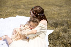 A tender embrace between mother and child sitting on a blanket in a sunlit grassy field.