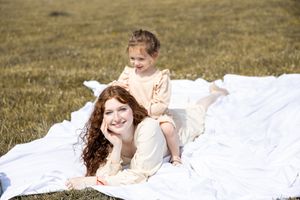 Two people in white clothing laying on a white blanket in a grassy field on a sunny day.