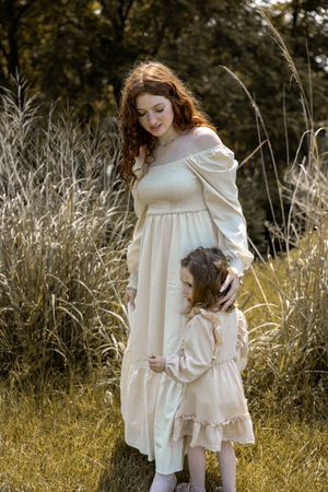 A dreamy outdoor portrait showcasing matching cream-colored dresses amid tall autumn grasses.