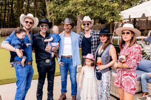 Friends and family gather outdoors at a sunny event wearing casual summer attire and sunglasses.