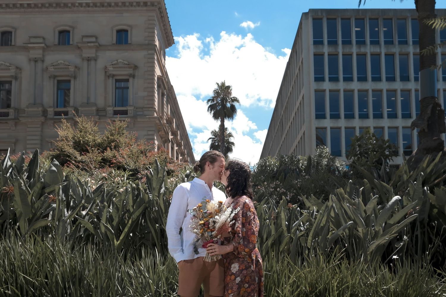 Wedding couple poses outside a Mediterranean style building under blue skies.