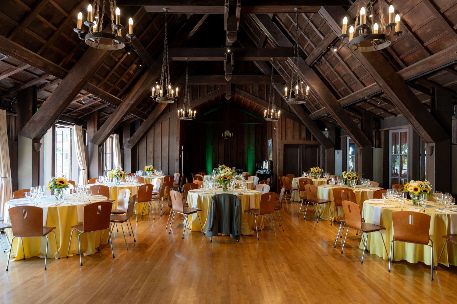 A panoramic view of an elegant rustic barn wedding venue with chandeliers and tables set for a reception.