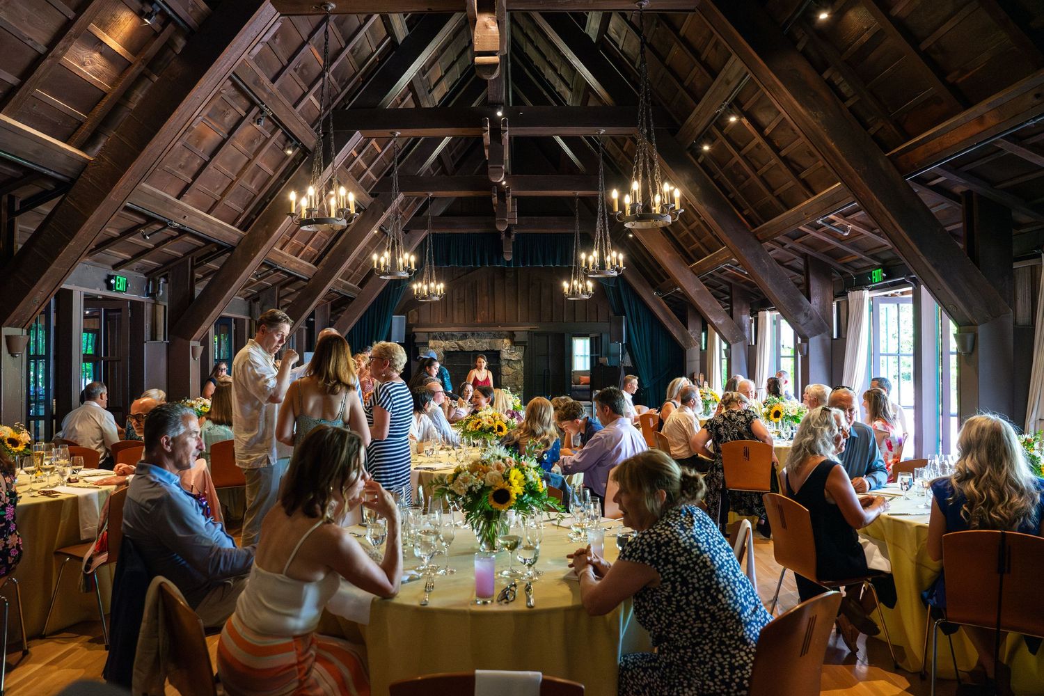 Wedding guests celebrate at a rustic reception venue with exposed wooden beams and elegant chandeliers.