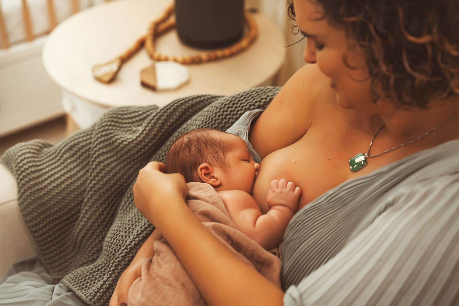A tender moment of breastfeeding under a cozy knit blanket in warm natural lighting.