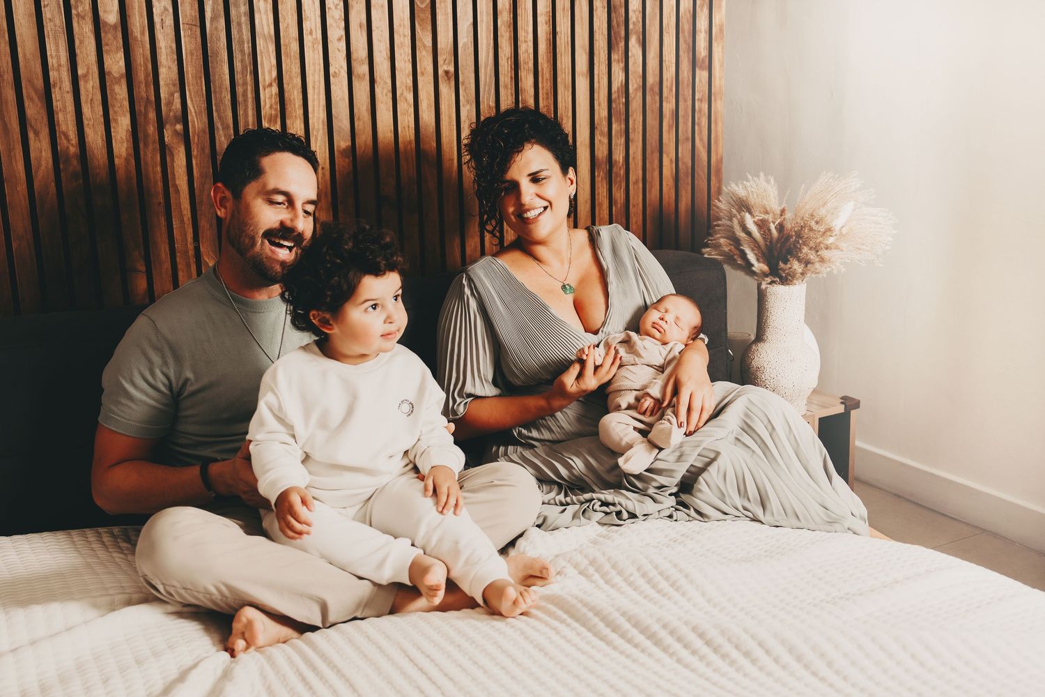A relaxed family moment on a bed with wooden paneling and neutral tones in the background.