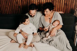 Family lounging together on bed with wood panel background in matching neutral outfits.