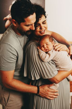 An intimate family moment as parents embrace their sleeping newborn baby indoors.