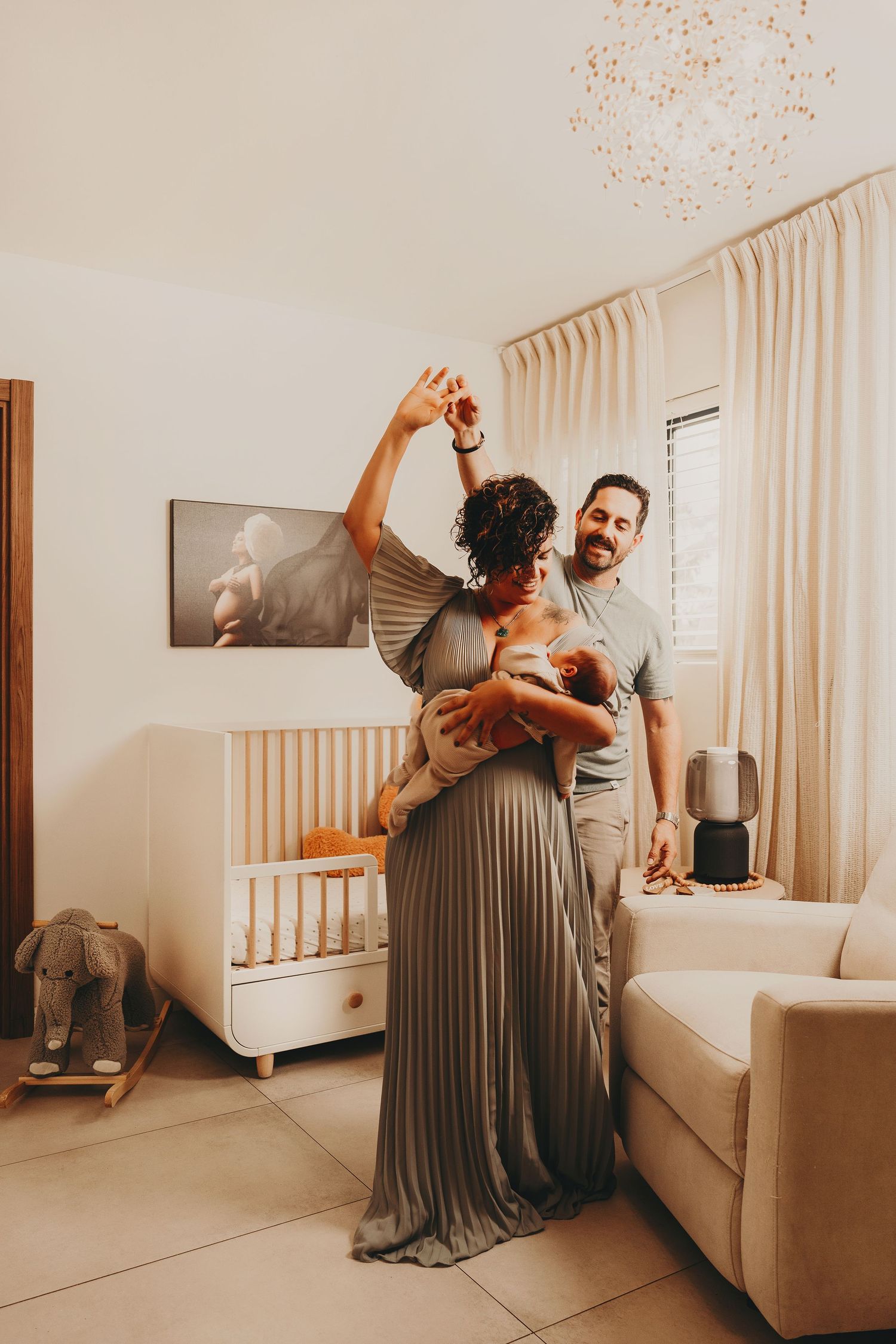 A couple dancing together while holding their baby in a cozy living room with neutral decor.