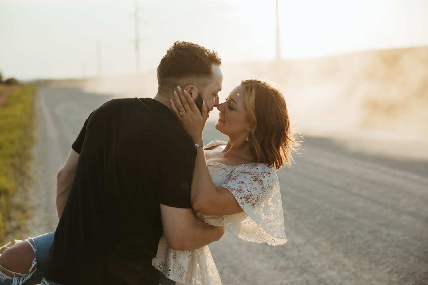 A couple shares a romantic moment at sunset on a dirt road in warm glowing light.