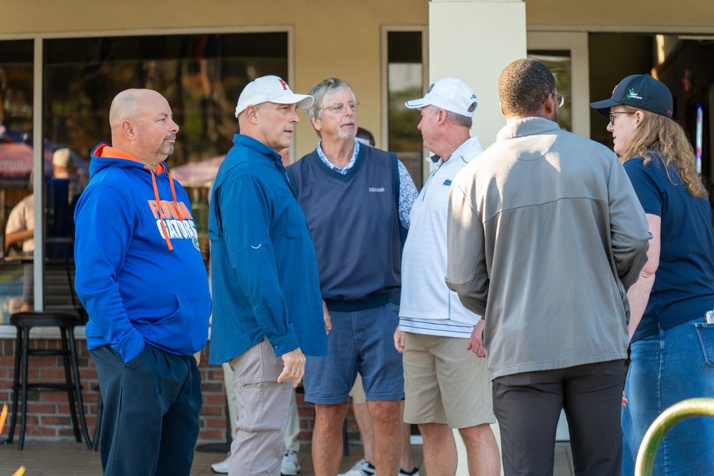 Group of men in casual attire having an outdoor conversation near a building on a sunny day.