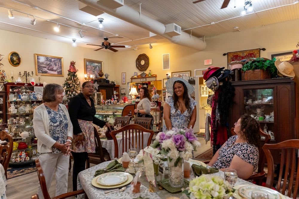 Women socializing in a charming antique shop with elegant table settings and holiday decorations.