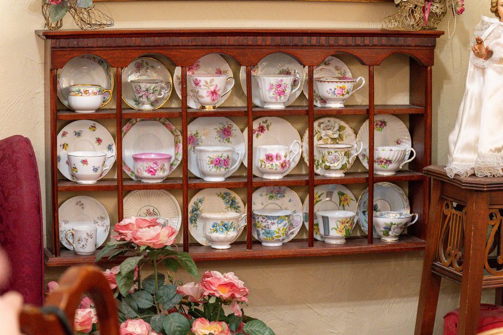 Wooden wall-mounted display shelf showcasing a collection of decorative floral teacups and saucers arranged in neat rows.