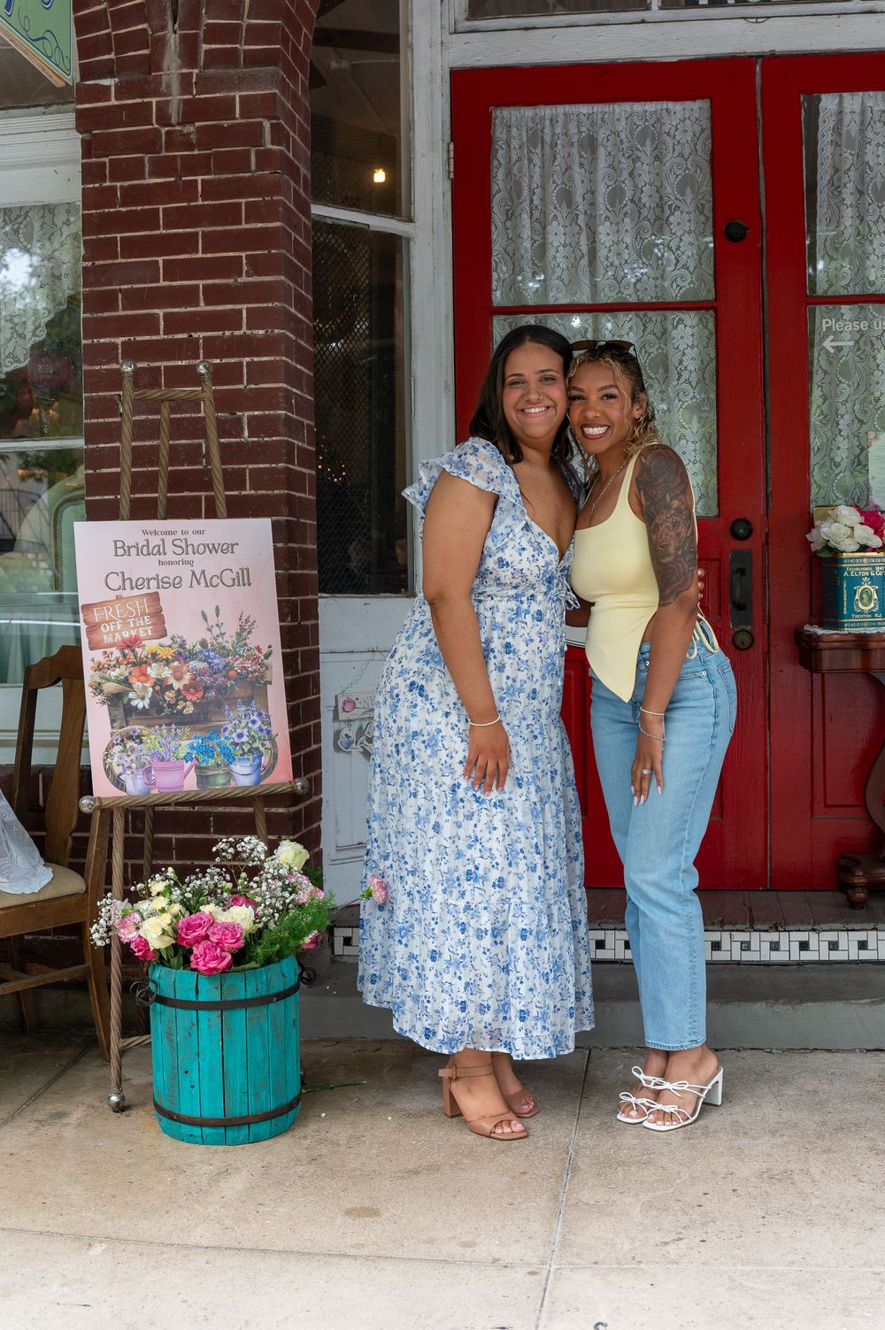 Two women pose smiling outside a shop entrance at a bridal shower for Charina McGill.
