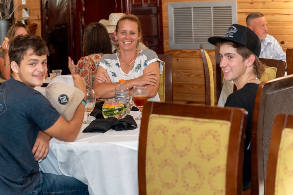 Three people sit around a restaurant table sharing a casual meal in a rustic wood-paneled dining room.