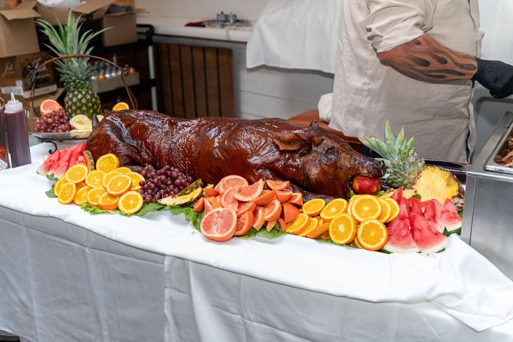 A whole roasted pig is displayed on a buffet table, garnished with colorful citrus and pineapple decorations.