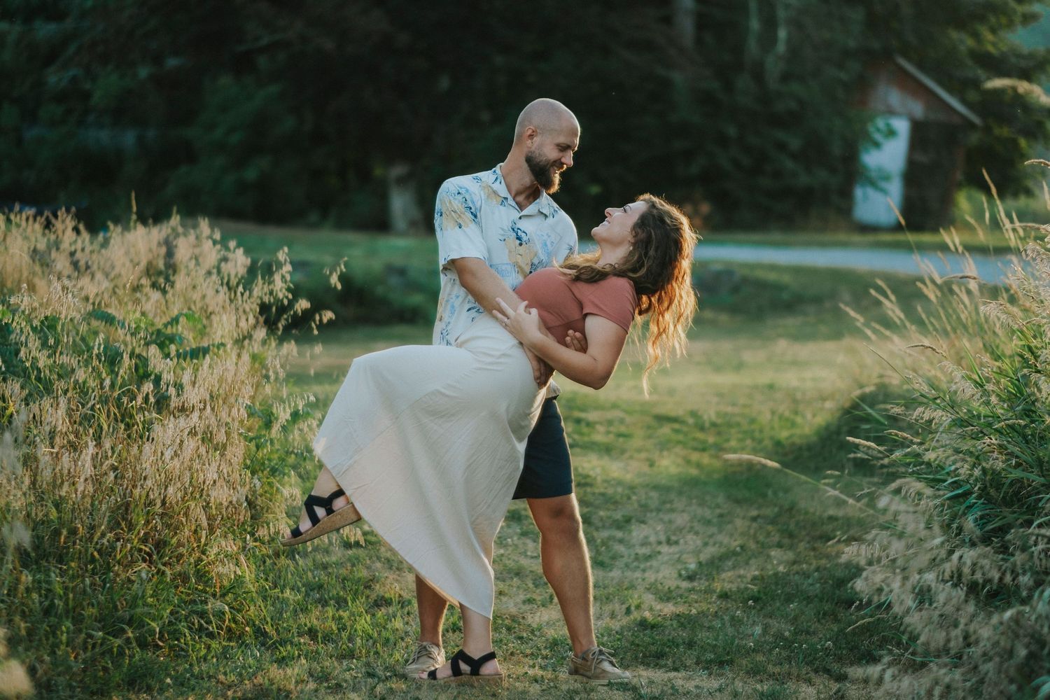 Romantic couple in flowy white outfits posing intimately in a serene outdoor garden setting at golden hour.