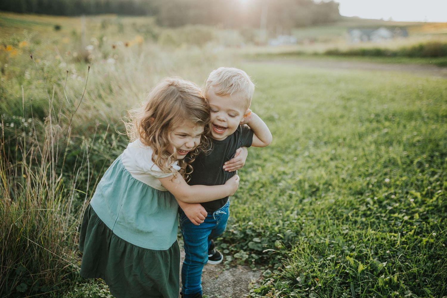 Two children playing and laughing together in a sunlit meadow.