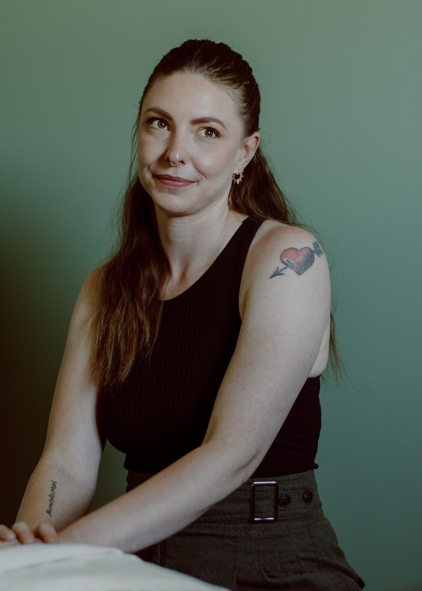 Headshot of a massage therapist in a calming space with a massage table and green accents.