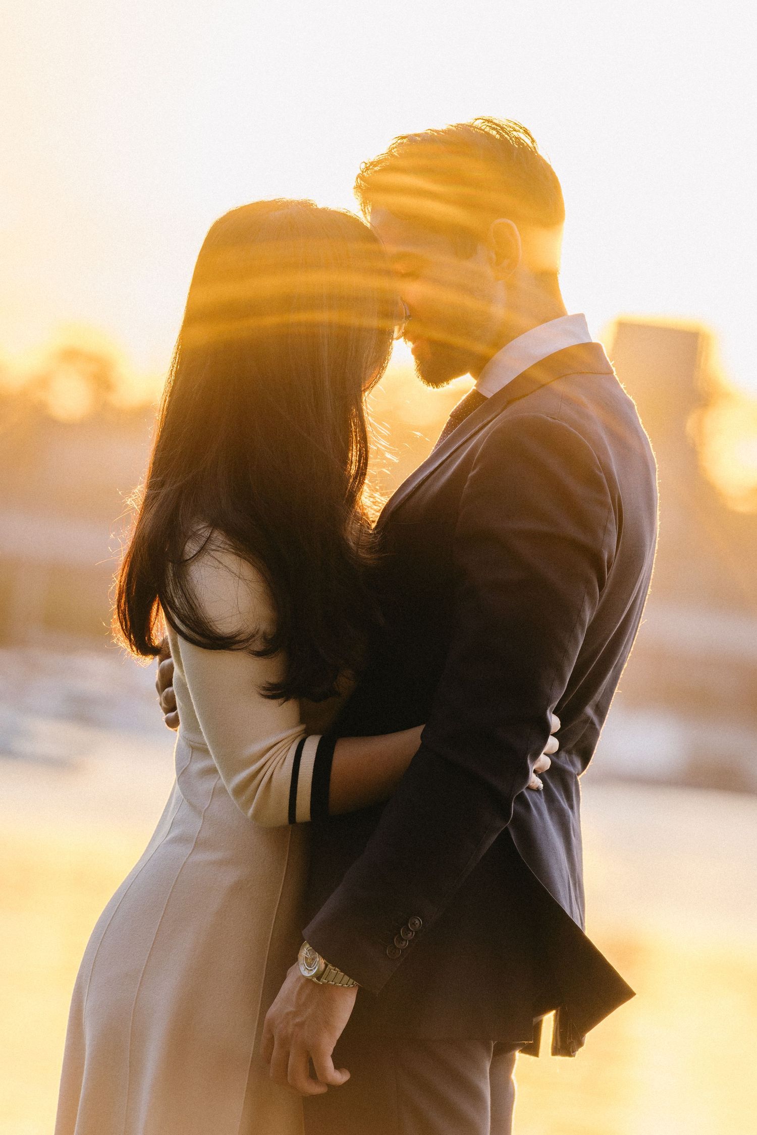Silhouetted couple embracing against warm golden sunset backdrop in romantic outdoor photoshoot sequence.
