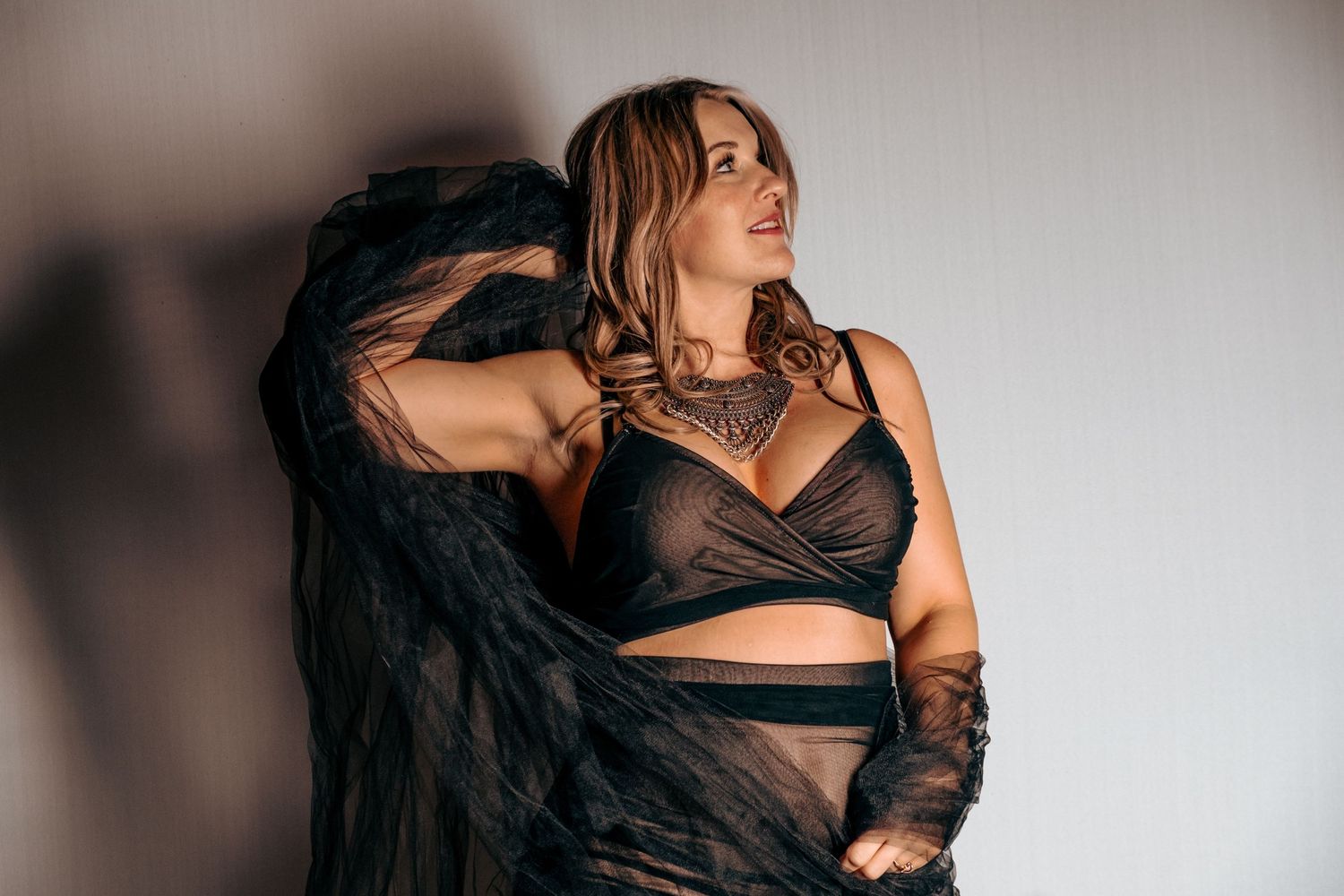 Fashion portrait featuring black outfit with sheer fabric against dramatic shadow backdrop.