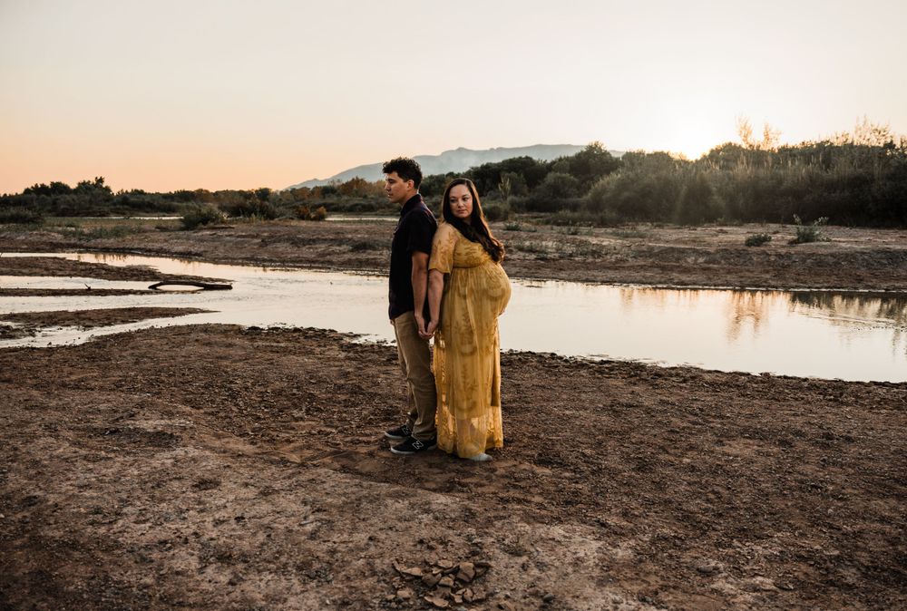 Desert landscape maternity photo with couple silhouetted against sunset water.