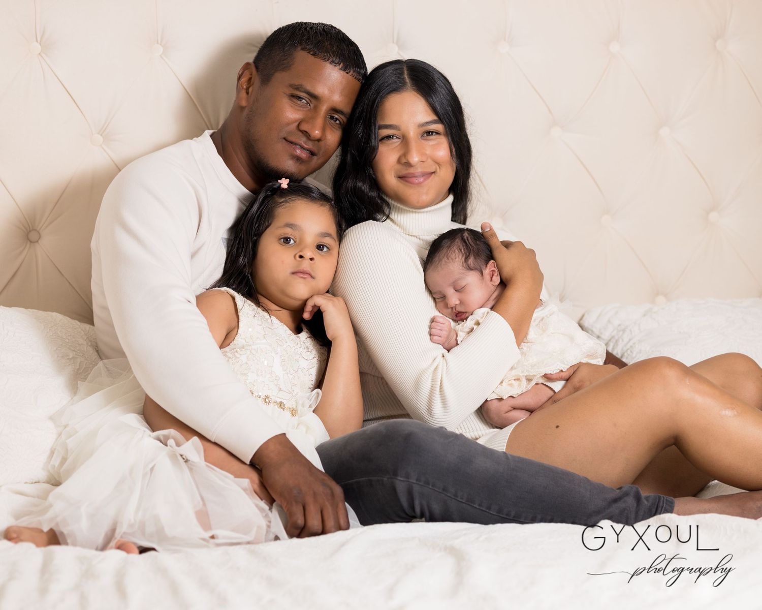 Beautiful family portrait in white clothing snuggling together on a light colored couch.