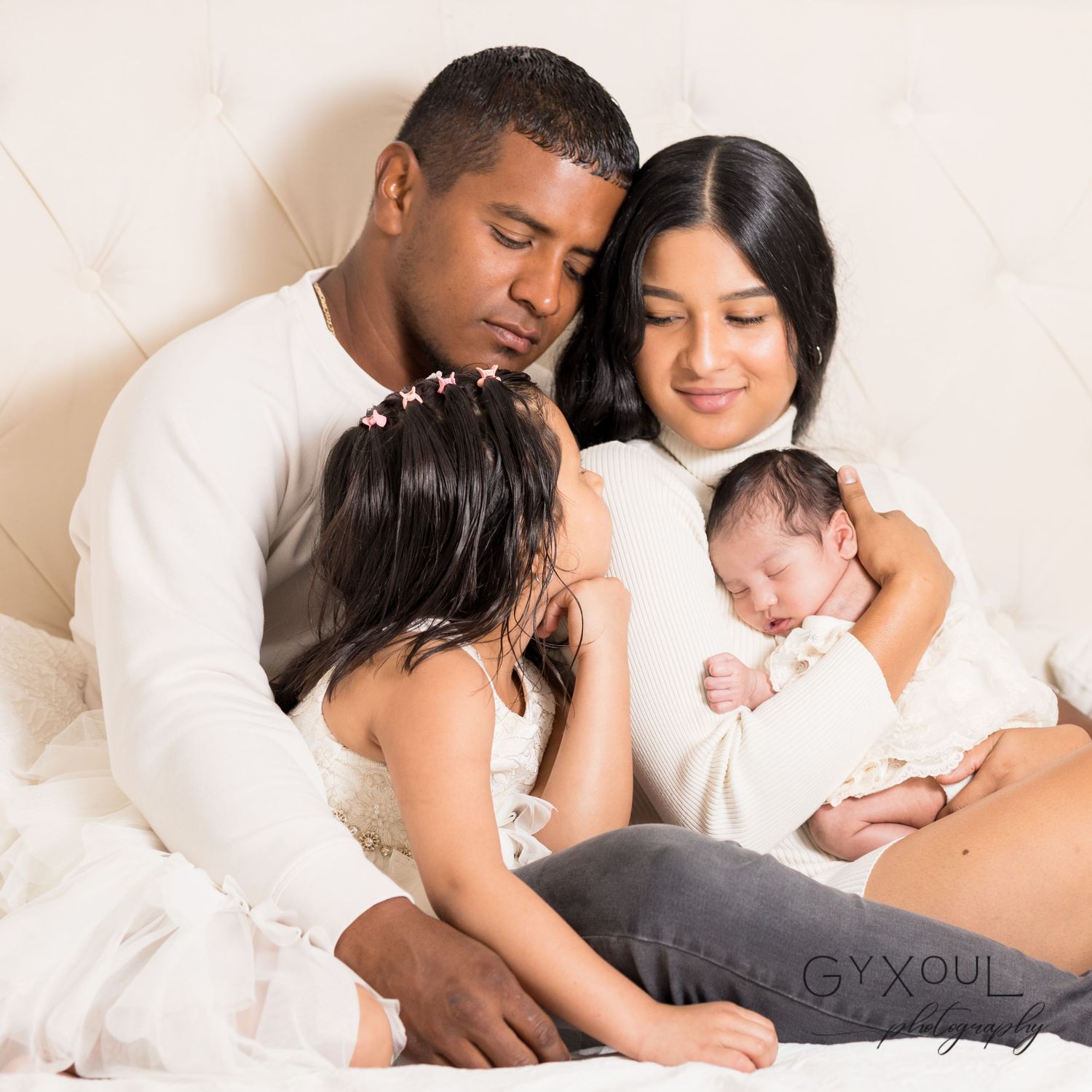 Family with newborn baby sharing an intimate moment together on white bedding.