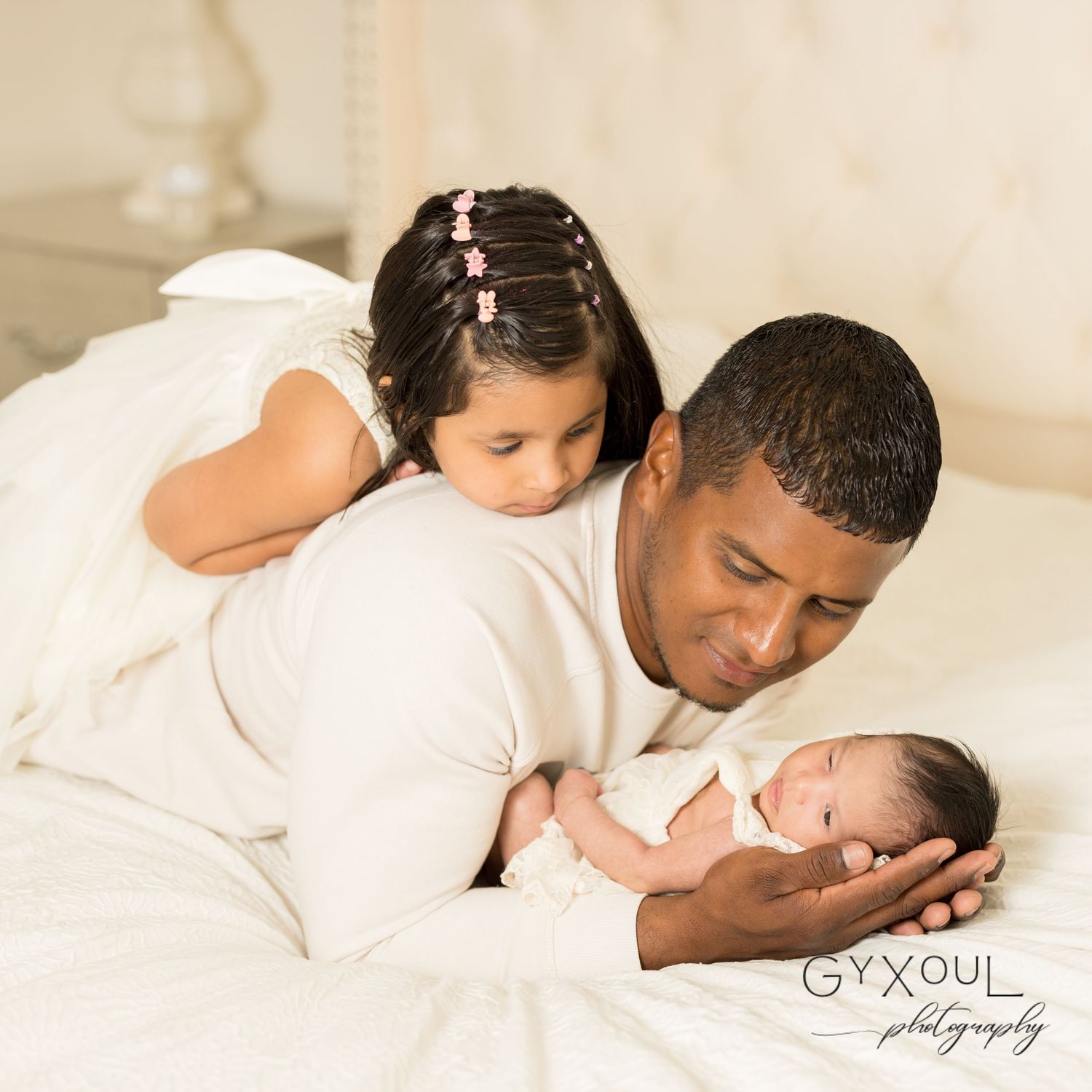 Sweet family moment with young child and newborn baby resting on white bedding.