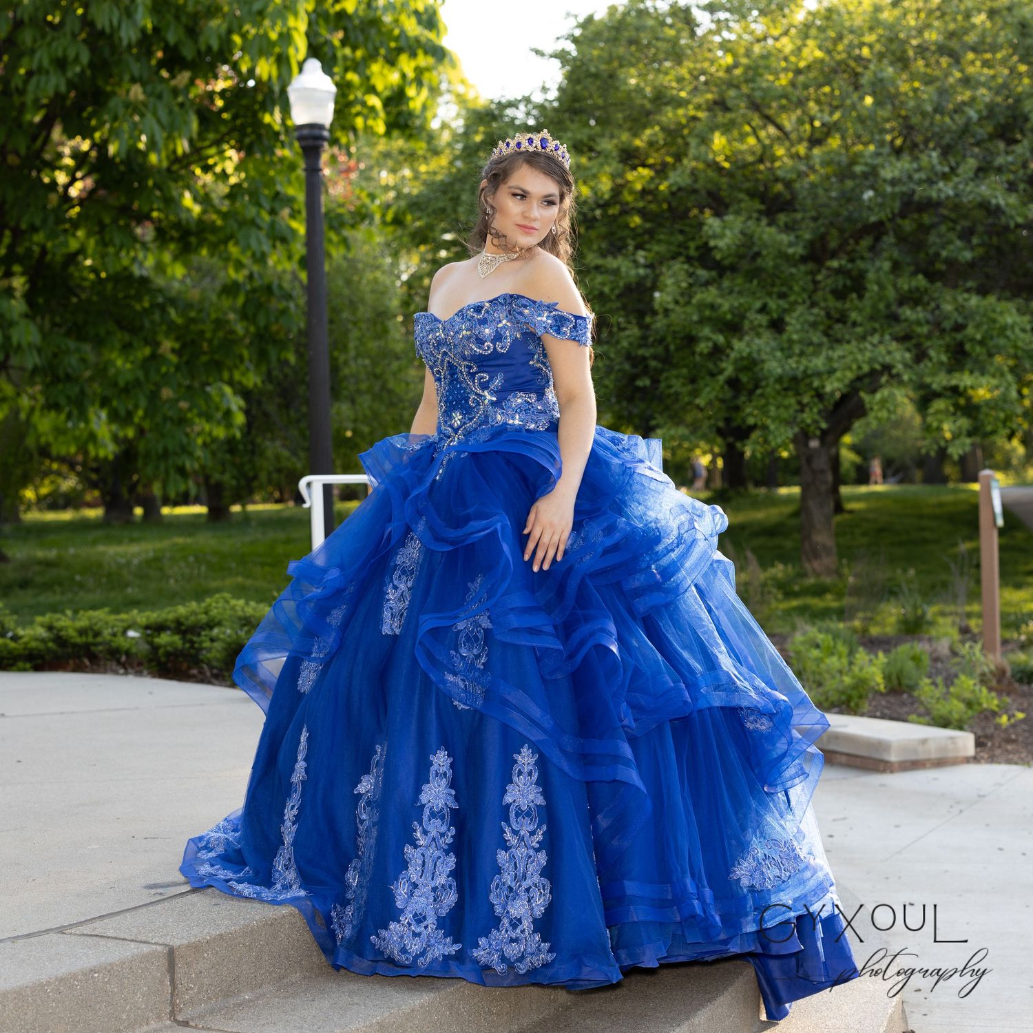 Majestic royal blue ball gown with lace appliques photographed in park setting with lamp post.
