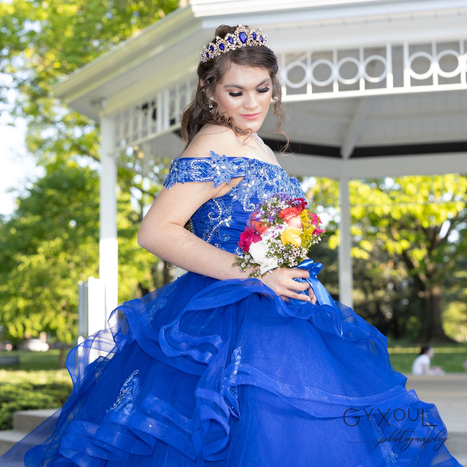 Royal blue ball gown with floral bouquet photographed in front of white gazebo.