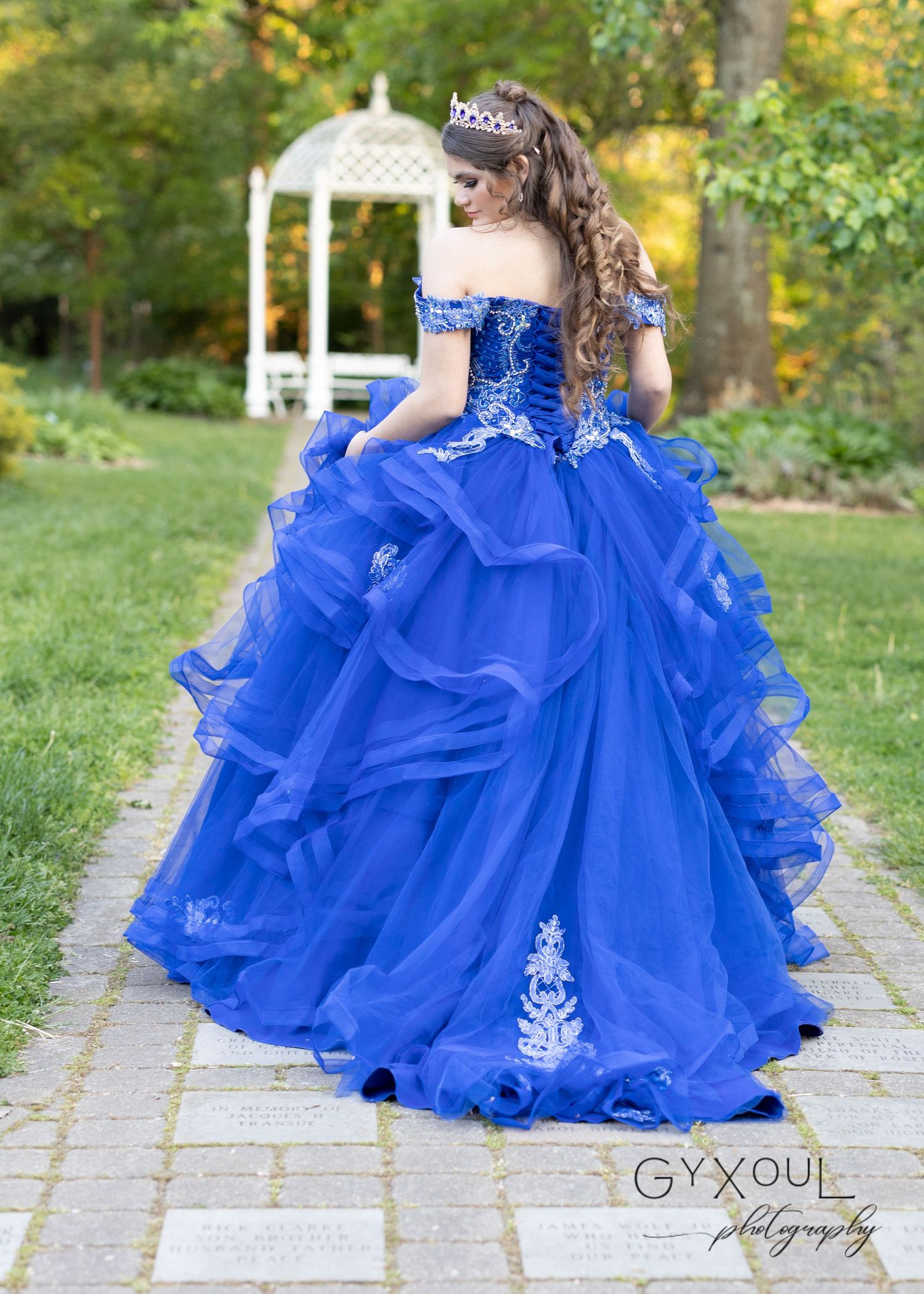 Dramatic royal blue ruffled ball gown photographed from behind with gazebo in background.