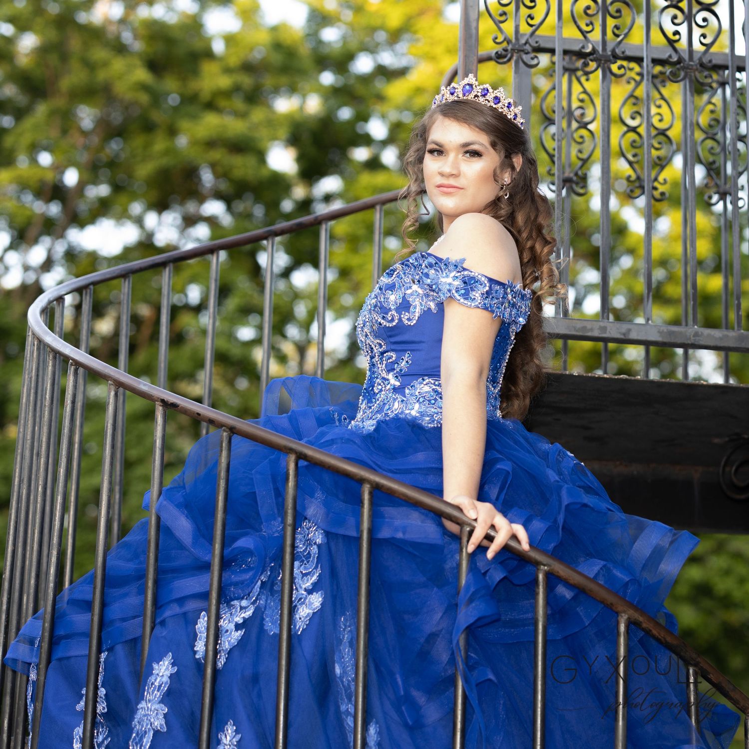 Ornate blue ball gown with embroidered details captured on spiral staircase with wrought iron railing.