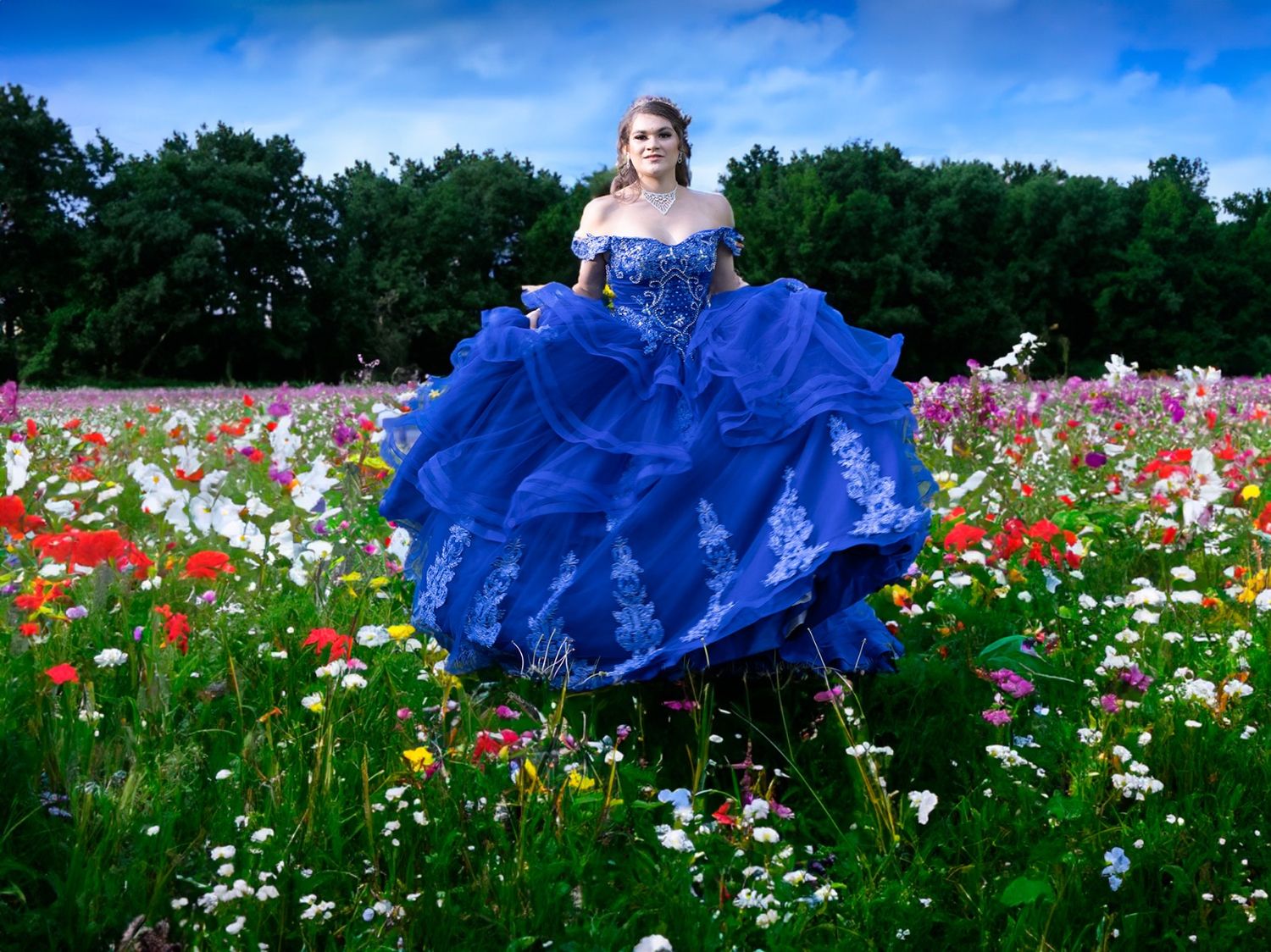 Elegant blue ballgown with intricate details photographed in a wildflower field on a sunny day.