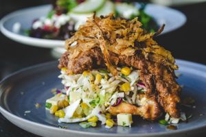 Crispy fried chicken served over coleslaw with corn on a gray plate with a side salad.