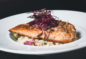 Seared salmon fillet served over creamy risotto, garnished with purple microgreens on a white plate.