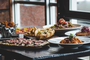 Spread of restaurant dishes including pizza, salads, and appetizers displayed on a wooden table.