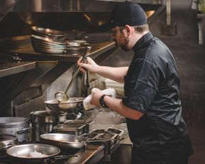 Professional chef in black uniform cooking in a busy commercial restaurant kitchen.