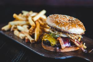 Loaded cheeseburger with bacon and toppings served with golden french fries on a dark platter.