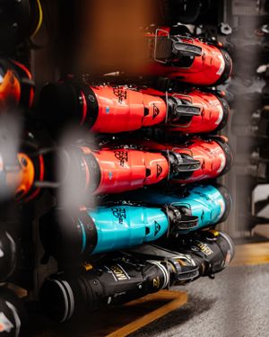 Colorful red and teal ski boots neatly stacked on a rental rack in a ski shop.