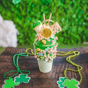 St. Patrick's Day green milkshake topped with Lucky Charms, gold coin, graham crackers, and festive shamrock decorations.