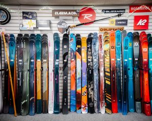 Colorful collection of ski brands including Armada, Rossignol, K2, and Blizzard displayed in a ski shop.