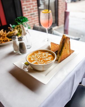 Creamy tomato soup with grilled sandwich served alongside a refreshing pink spritz cocktail.