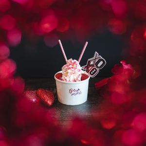 Valentine's Day ice cream cup with pink whipped cream and XO decorative picks surrounded by red bokeh roses.