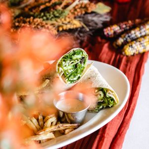 Fresh veggie wrap with crispy fries and dipping sauce served on a white plate with autumn decor.