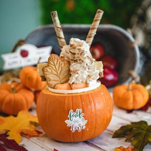 Autumn pumpkin bowl filled with creamy milkshake, whipped cream, leaf cookies, and wafer straws for fall season.