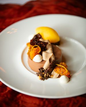 Elegant chocolate dessert with candied orange, meringue, and mango sorbet on white plate.