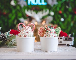 Festive Christmas ice cream cups topped with whipped cream, candy canes, and holiday decorated cookies in snowy setting.